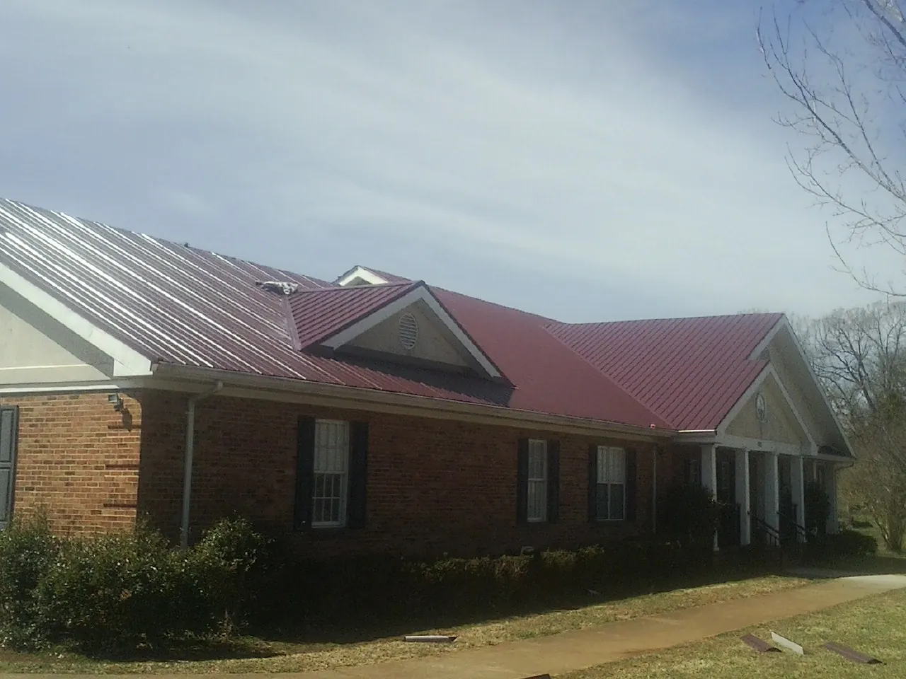 Red metal roof with gabled entries on a long brick building, from a Hail Damage Roof Repair job in Coldwater