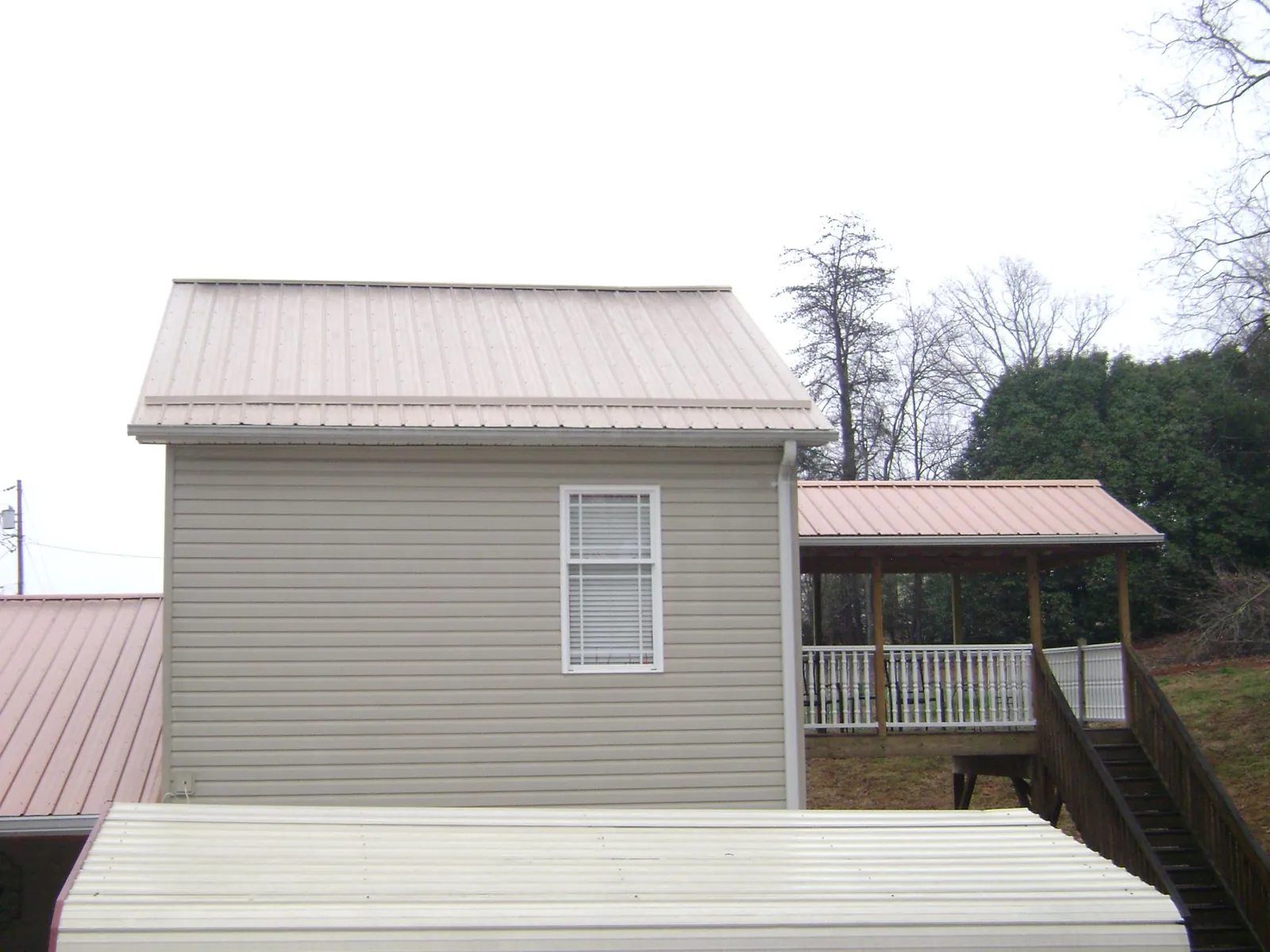 Tan metal roofs on a two story addition and attached porch, from a Roof Replacement job in Coldwater